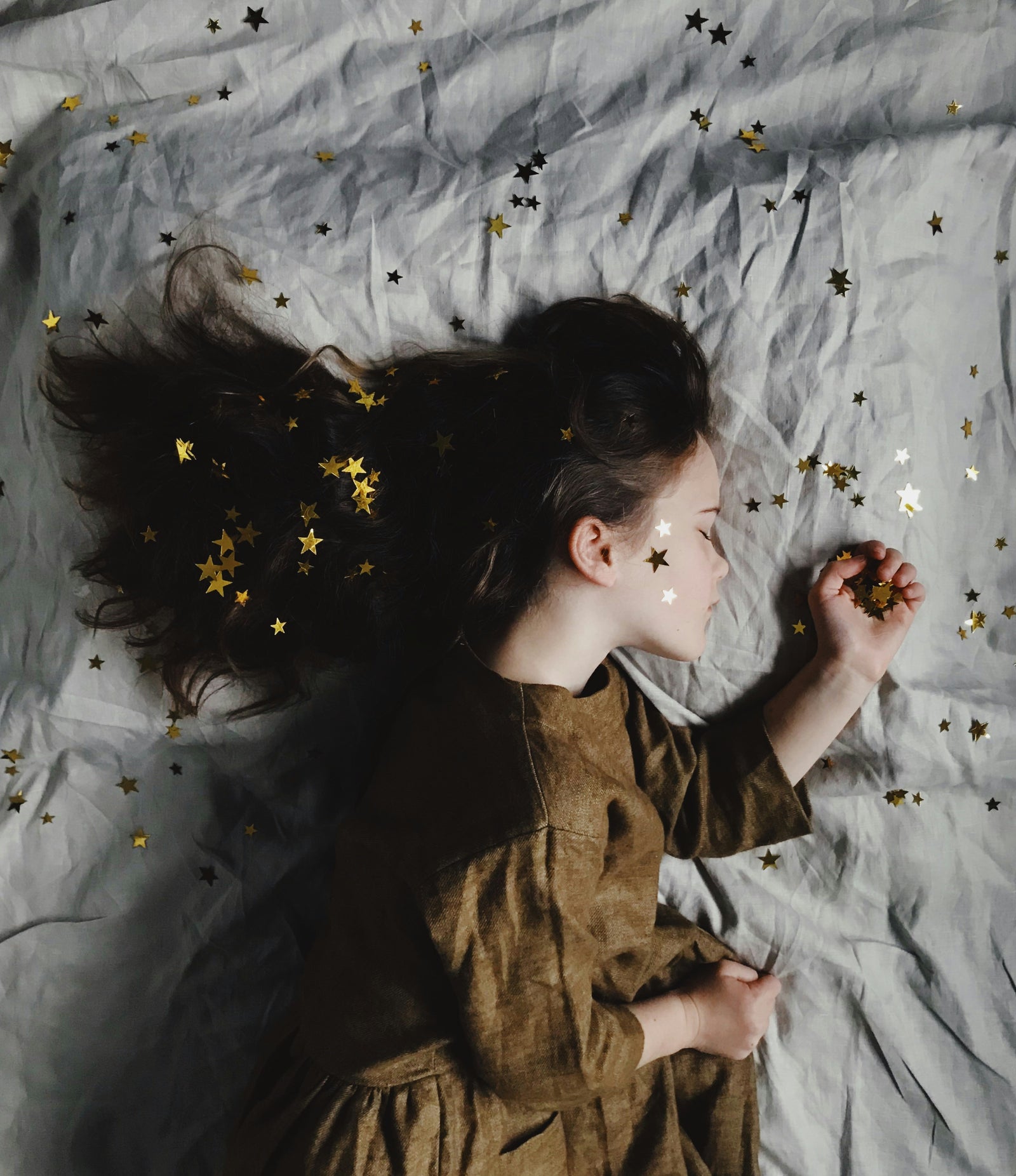 Mädchen schläft auf einem Bett mit kleinen, herumfliegenden, goldenen Sternen