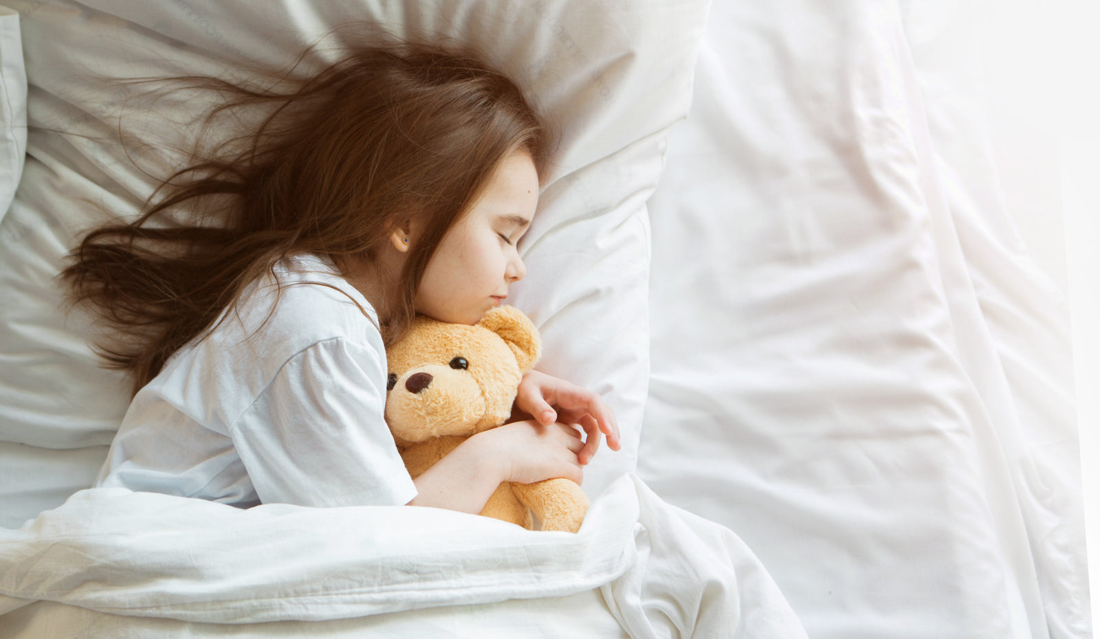 Kind schläft im Bett mit Kuscheltier