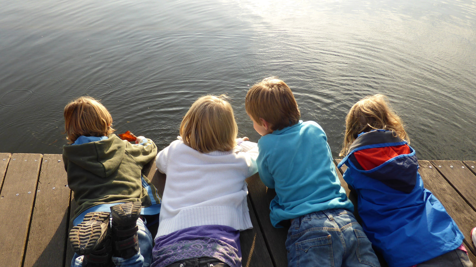 Vier Kinder liegen auf einem Steg und schauen auf einen See