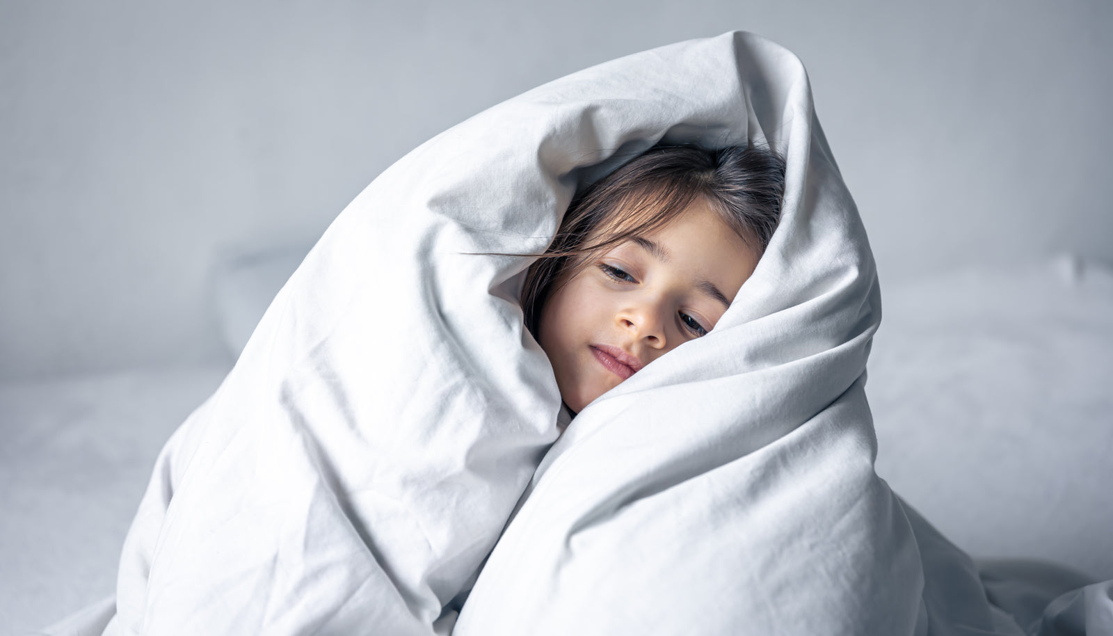 Kleines Mädchen eingekuschelt in einer Daunendecke