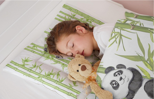 Ein Kind schläft in einem Bett auf einem Kopfkissen und dem Panda Bettbezug von Koru Kids
