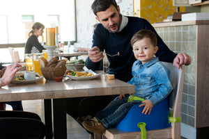 Ein Vater füttert sein Kind während es auf einer Sitzerhöhung von Koru Kids, dem Toddler Booster sitzt